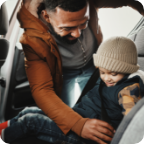 A father buckles his young child into the backseat of his vehicle.  